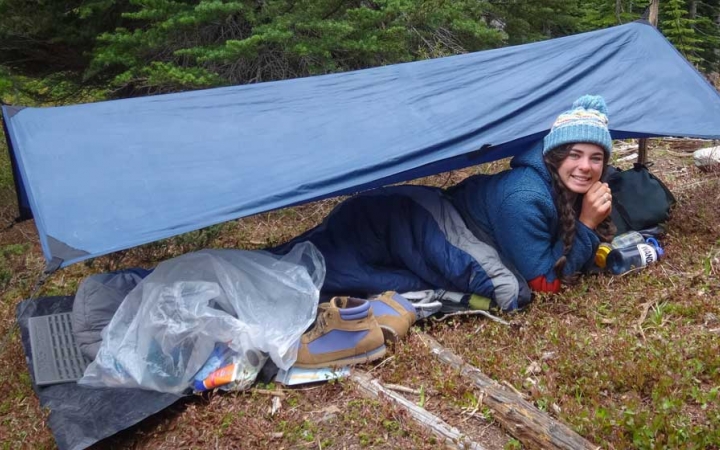 an outward bound student smiles from under their shelter while on solo